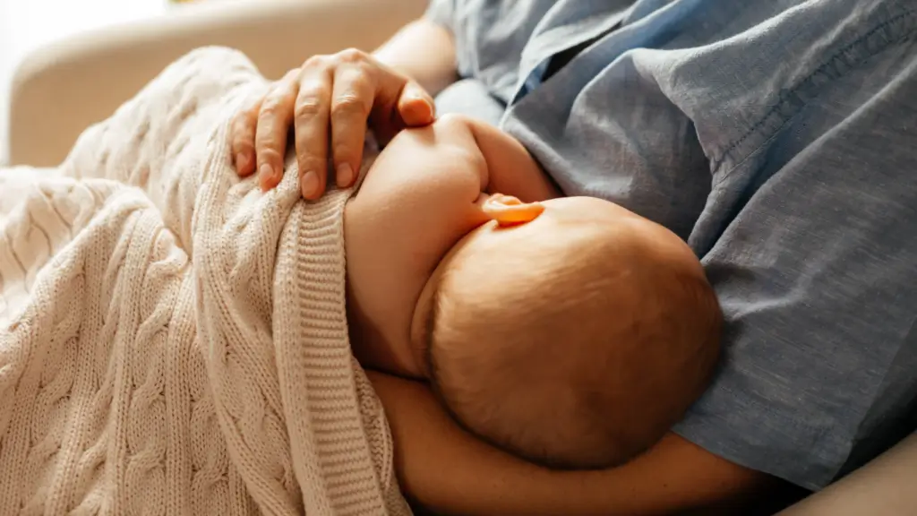 Mother breastfeeding baby under cozy blanket.